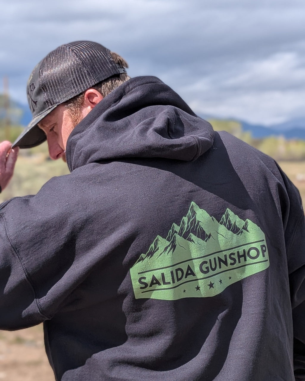 Close-up of the green Salida Gunshop mountain logo on the back of the hoodie with mountains behind